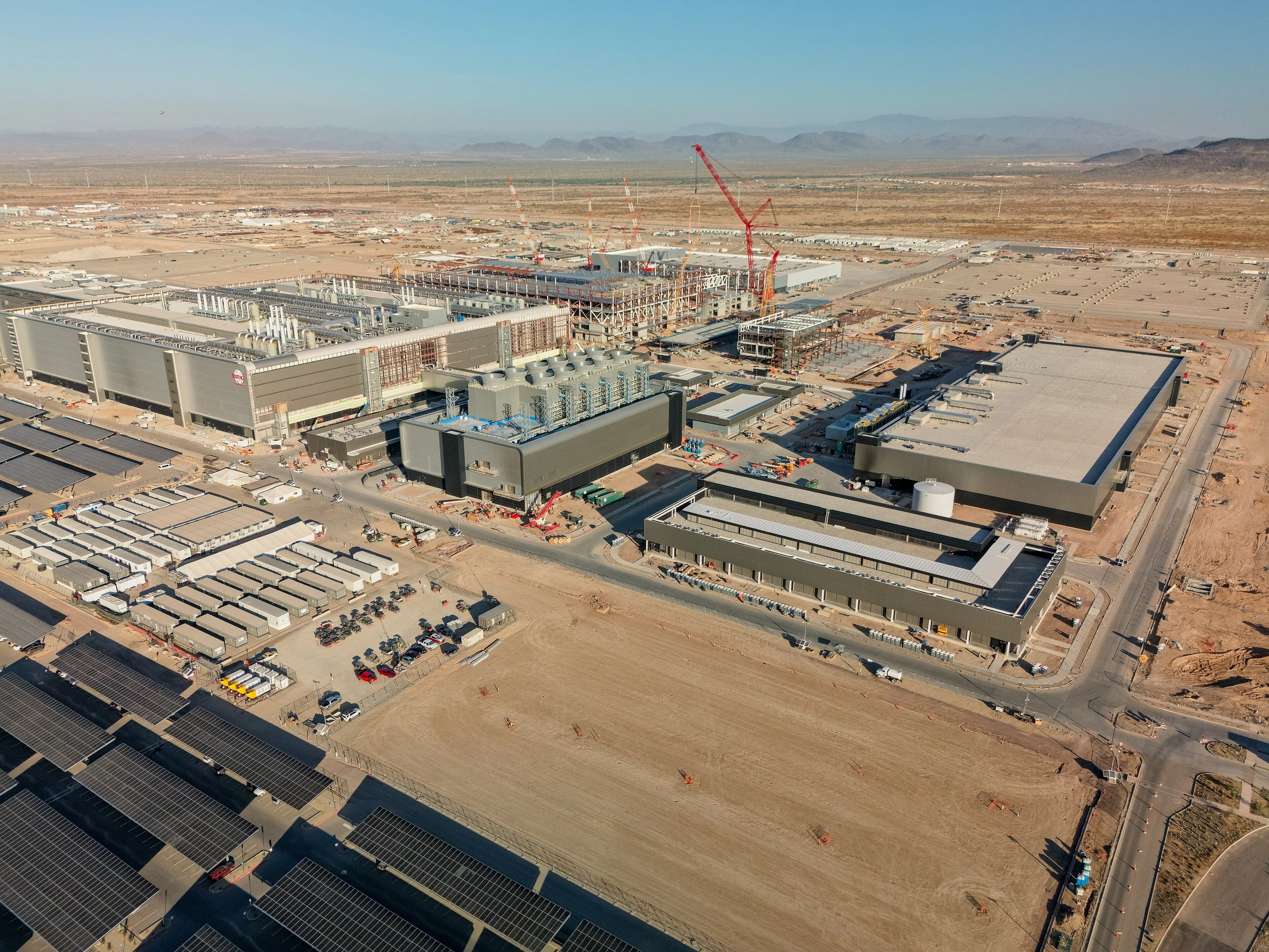 Aerial view of TSMC’s Fab 21 campus under construction in Phoenix, Arizona, showing factory buildings, cranes, utility infrastructure, and surrounding desert.