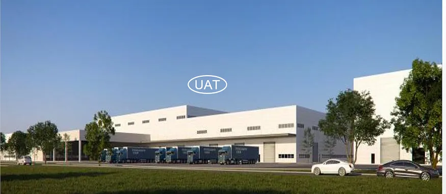 Official rendering of a United Alloy-Tech manufacturing facility with the UAT logo, loading bays, trucks, cars, and surrounding greenery.